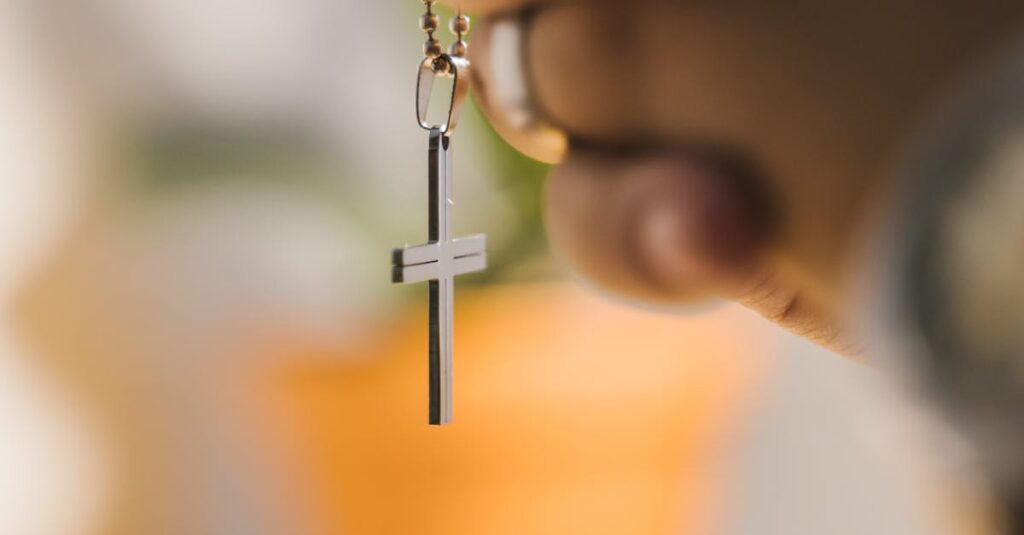 Close-up of hands clasped in prayer holding a cross pendant with blurred background.